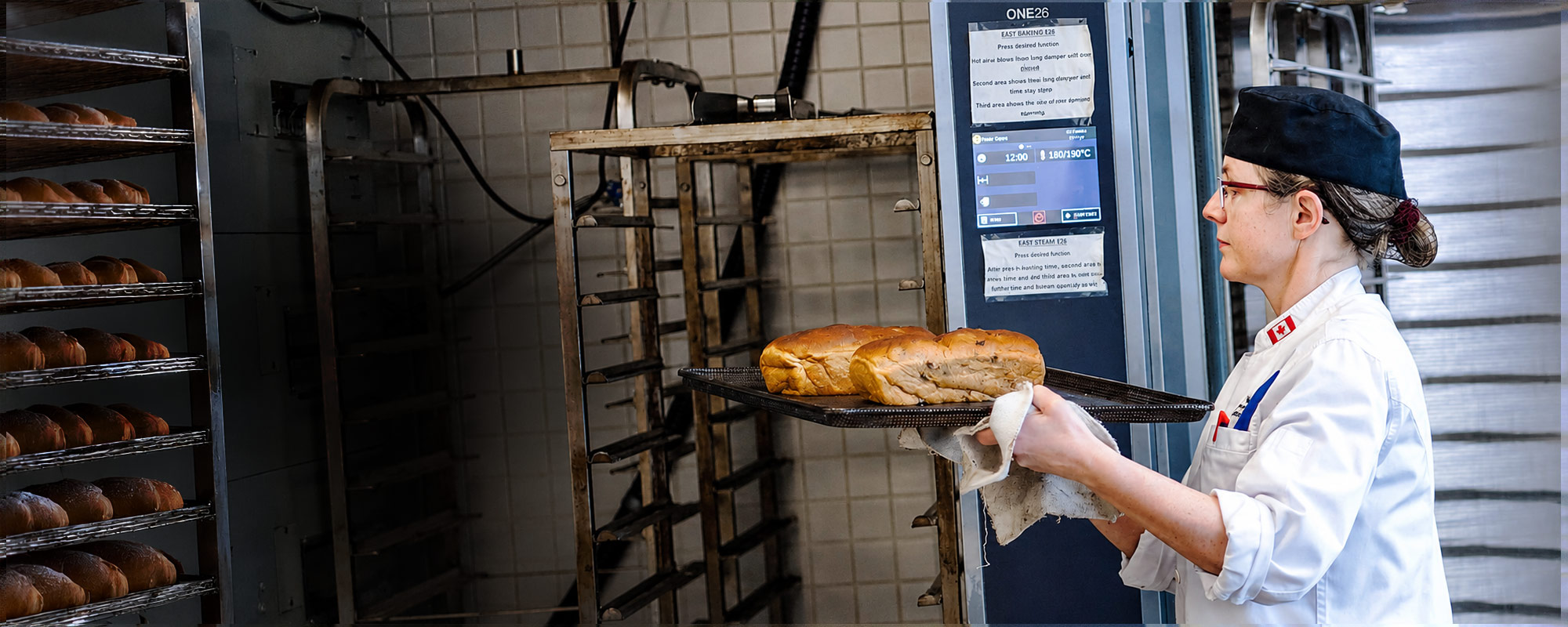 An artisan baking student carrying fresh bread from the oven.