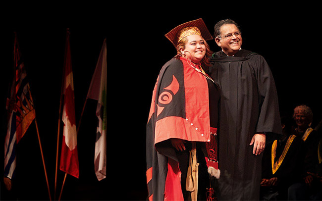 Indigenous graduate in full regalia representing her indigenous heritage posing with a college official