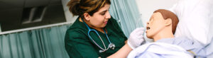 A nursing student practices inserting an airway tube into a patient training mannequin.
