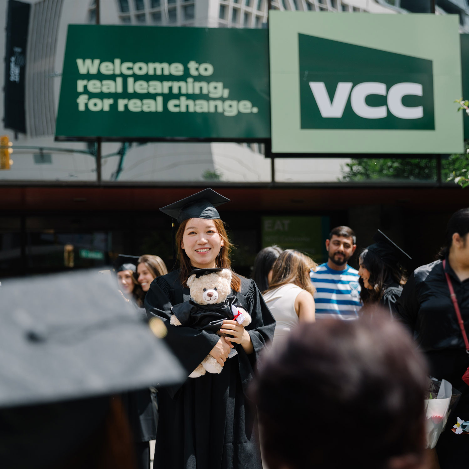 A VCC grad wearing her full regalia, standing in front of the entrance of the Downtown campus.