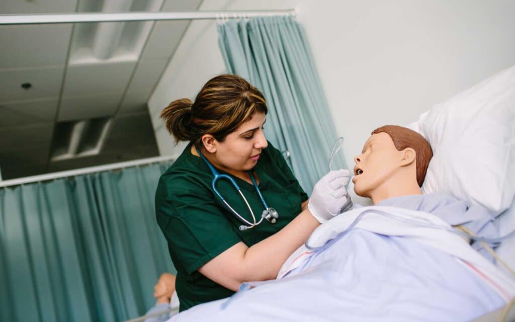Nursing student in a hospital simulation classroom working on a dummy