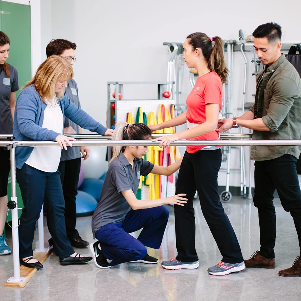 Occupational therapy students assisting a client with gait training using parallel bars, practicing mobility skills.