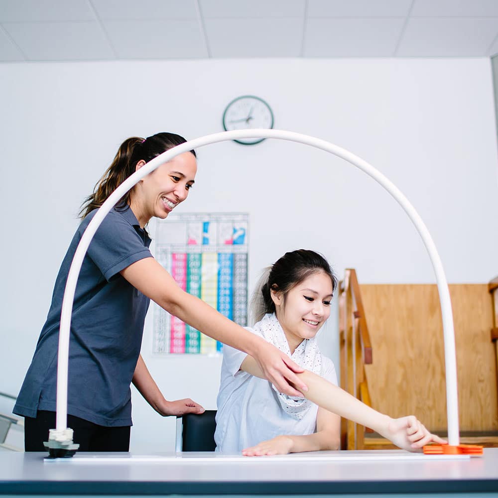 An occupational therapist assisting a client with an arm stretch exercise using a curved rehabilitation device.