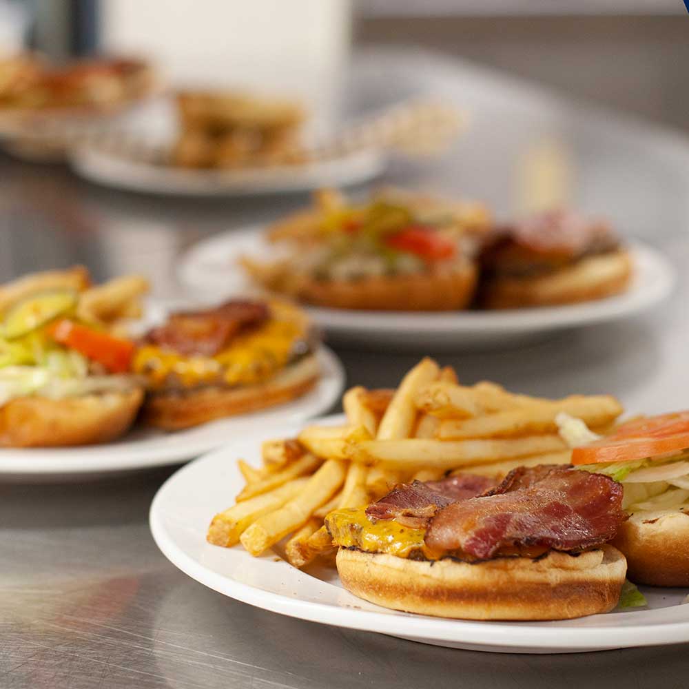 A freshly prepared bacon cheeseburger served with a side of golden fries on a white plate.