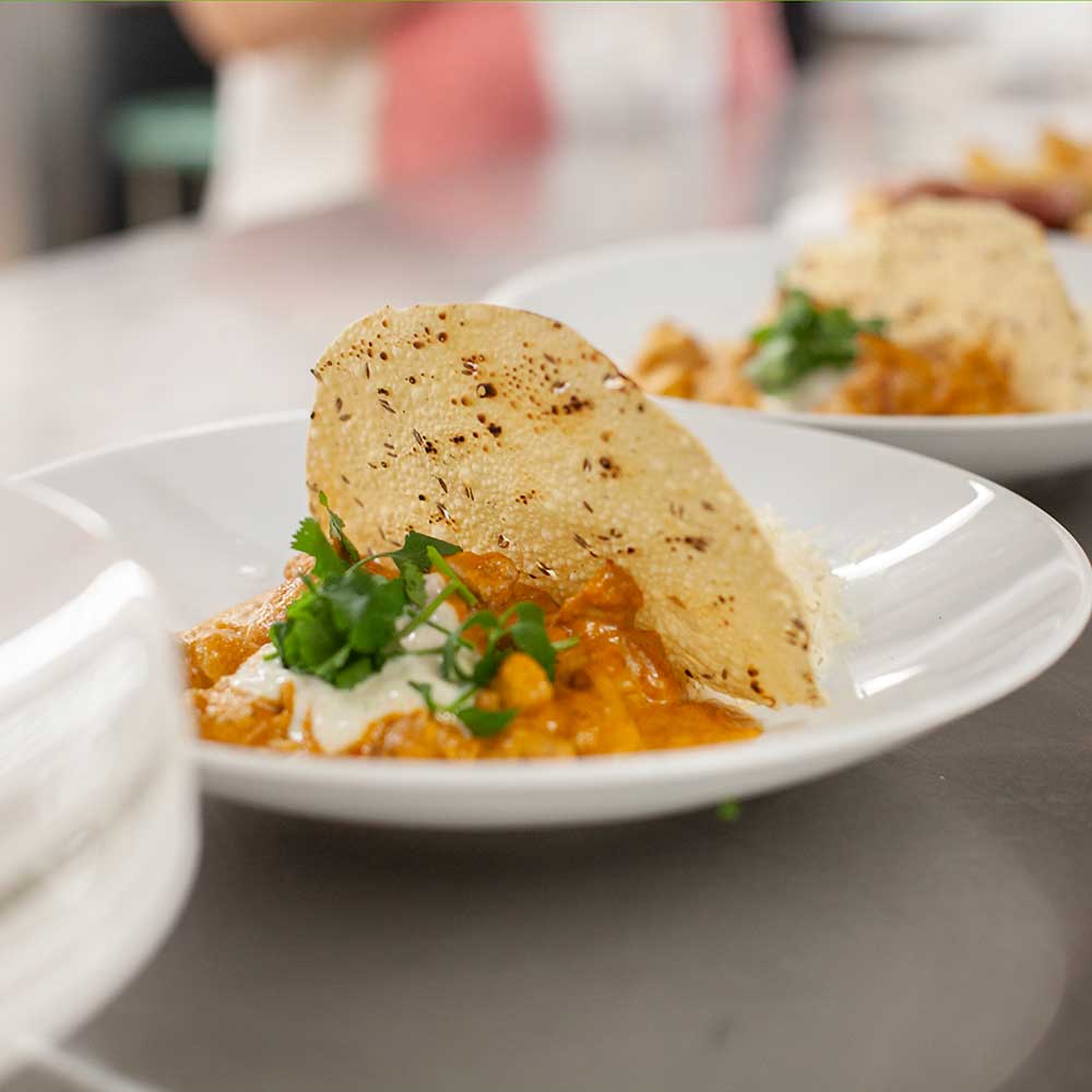 A bowl of creamy butter chicken garnished with fresh cilantro and served with basmati rice and a crispy papadum.