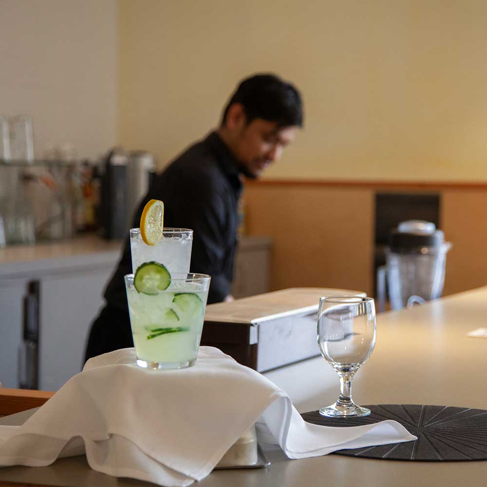 Refreshing iced cocktails garnished with lemon and cucumber slices sitting on a service bar.
