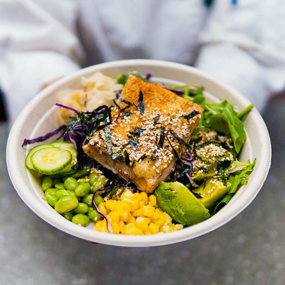 A colorful salmon poke bowl filled with edamame, corn, avocado, cucumber, and sesame seeds.