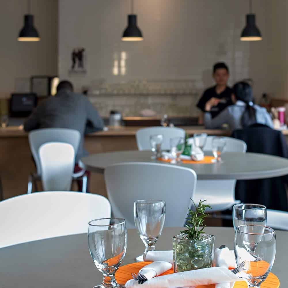 A contemporary bistro setting with elegant table arrangements in the foreground and a person sitting at a service counter in the background.
