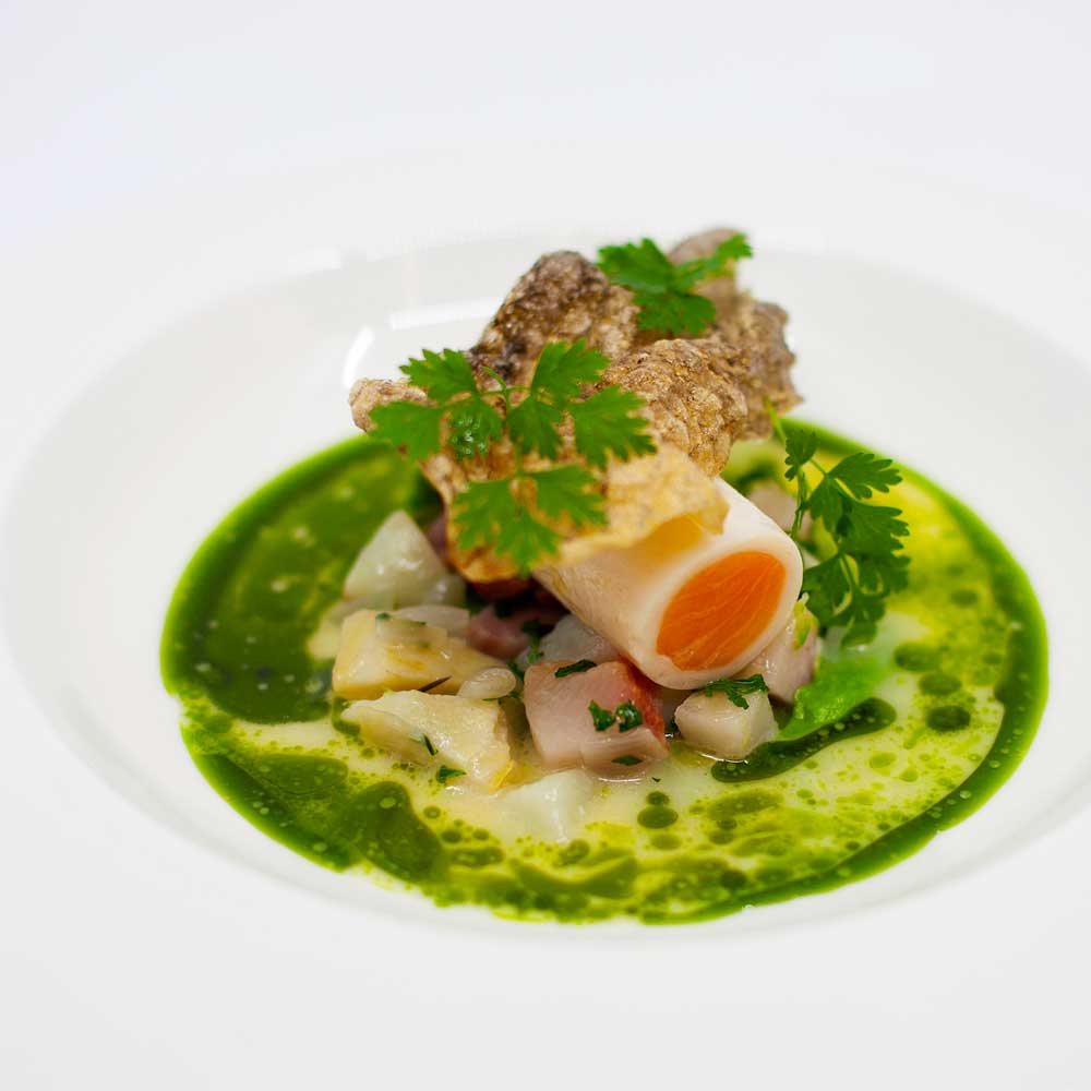 A sophisticated seafood arrangement centered around a carrot-filled roll in a herb-infused broth.