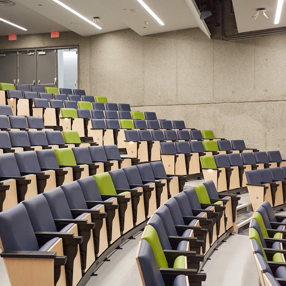 A modern tiered auditorium featuring rows of blue and lime green upholstered seating against a minimalist concrete wall.