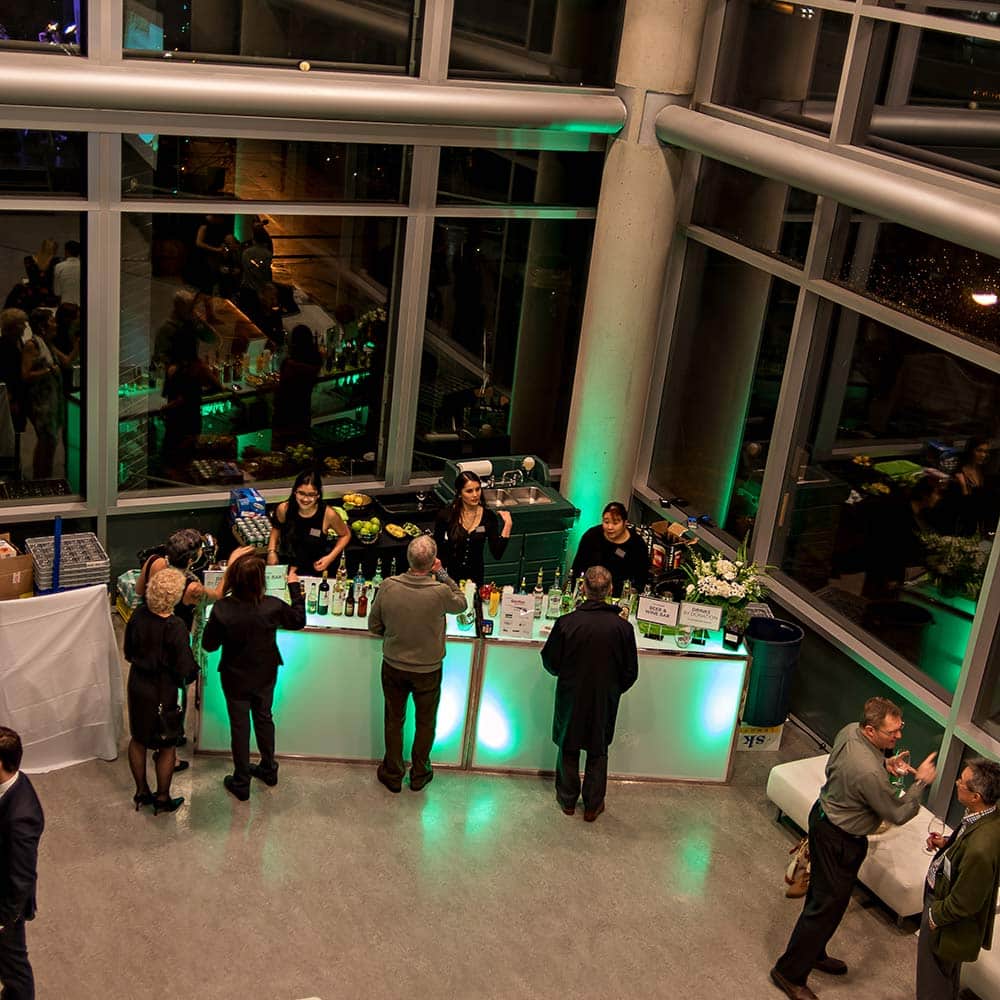 A high-angle view of a sleek, glowing event bar where staff are serving guests during an evening reception.