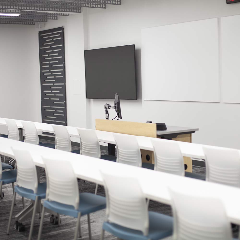 A contemporary classroom setup with rows of white desks and chairs facing a digital screen and whiteboards.