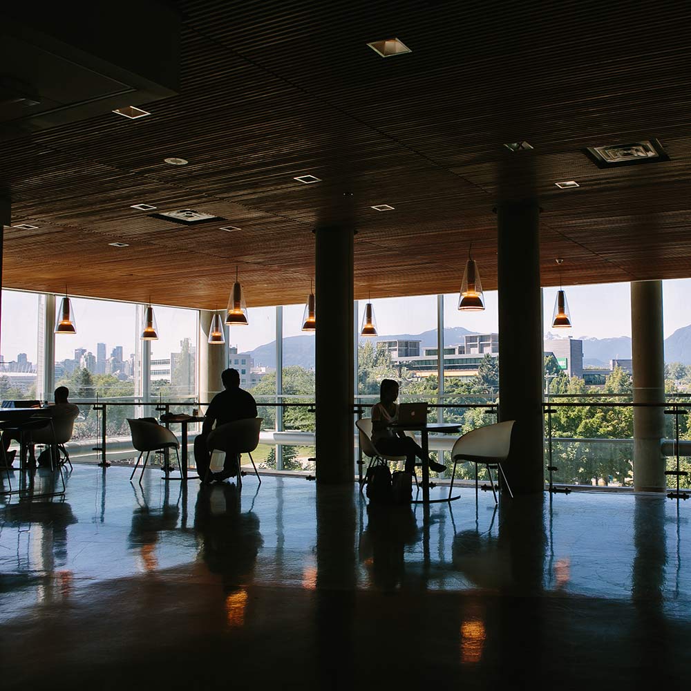 A sunlit, modern lounge featuring hanging pendant lights and floor-to-ceiling windows with a scenic view of a city and mountains.