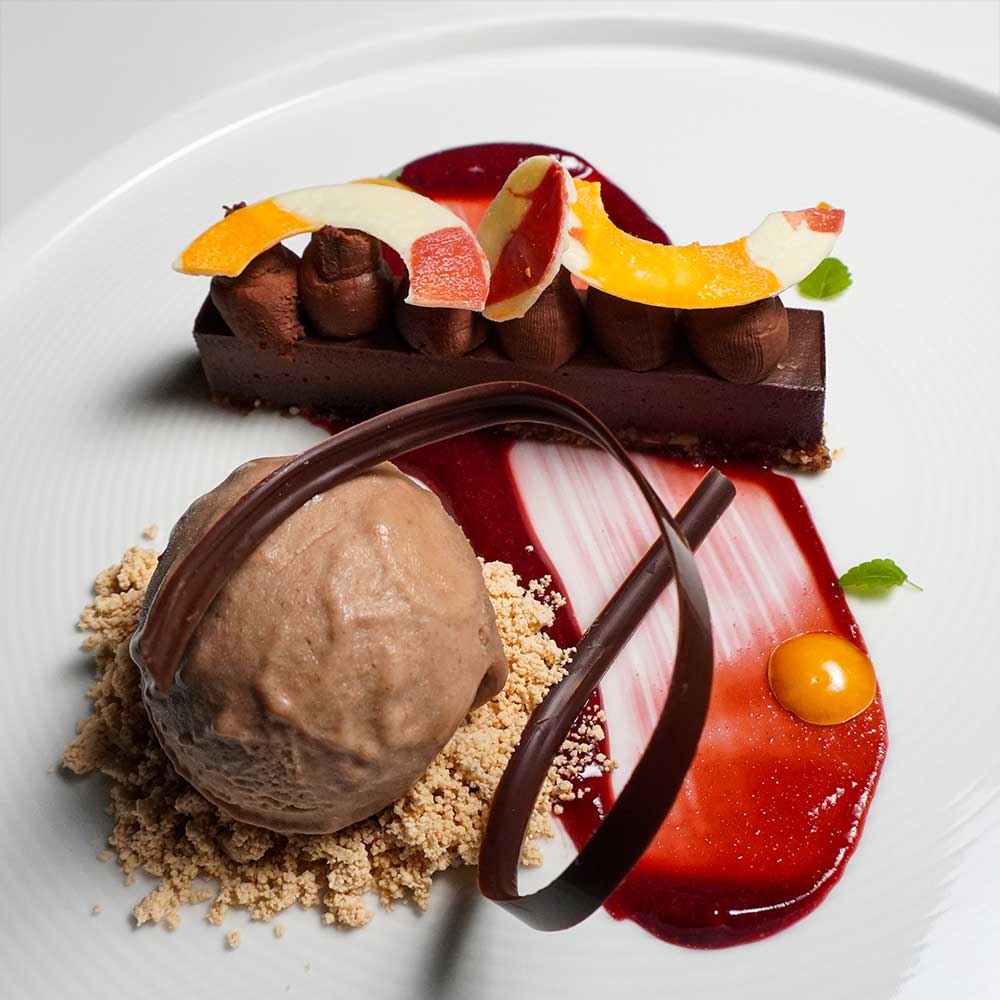 A sophisticated chocolate ganache bar served with a scoop of hazelnut gelato, vibrant berry coulis, and delicate chocolate curls.