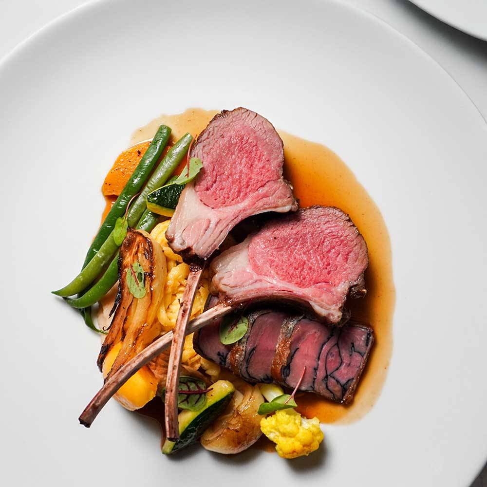 Perfectly seared lamb chops served medium-rare over a medley of roasted seasonal vegetables and jus.