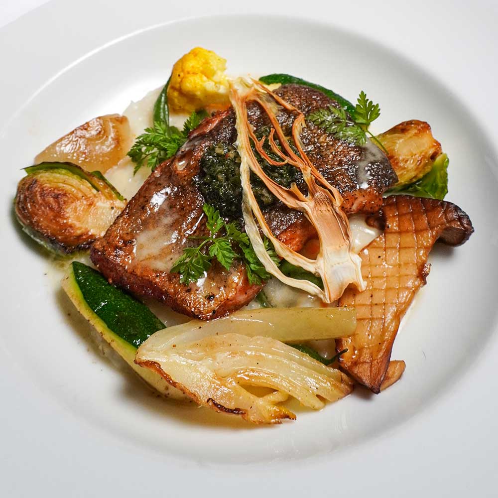 A pan-seared salmon fillet accompanied by roasted Brussels sprouts, king oyster mushrooms, and a light herb butter sauce.