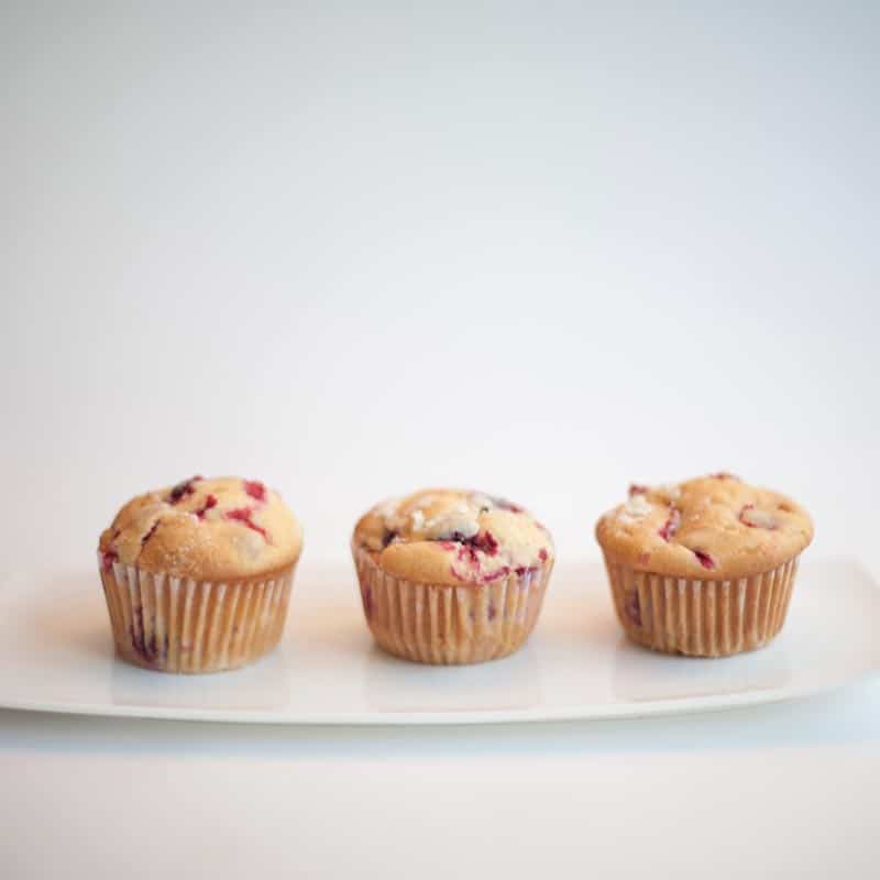 Three golden berry muffins lined up on a white rectangular plate against a clean white background.