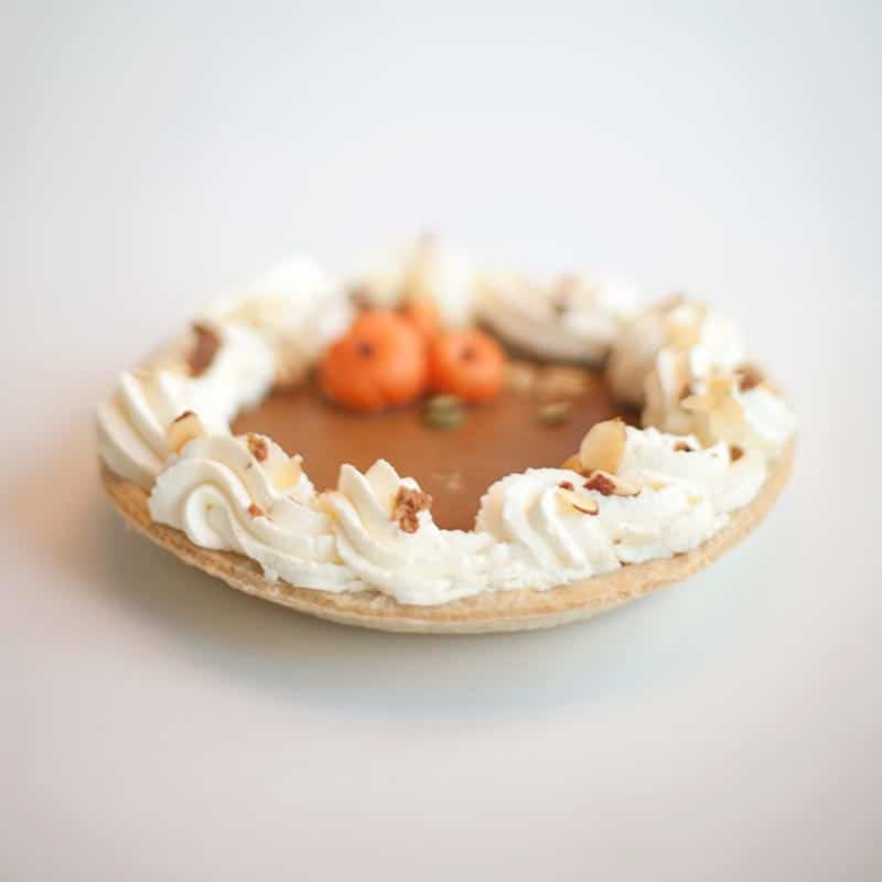 A freshly baked pumpkin pie with a whipped cream with a dusting of almond slivers.
