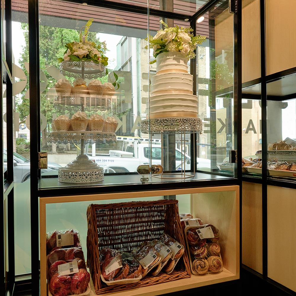 An elegant white multi-tiered wedding cake and matching cupcakes displayed in a glass case with floral decorations.