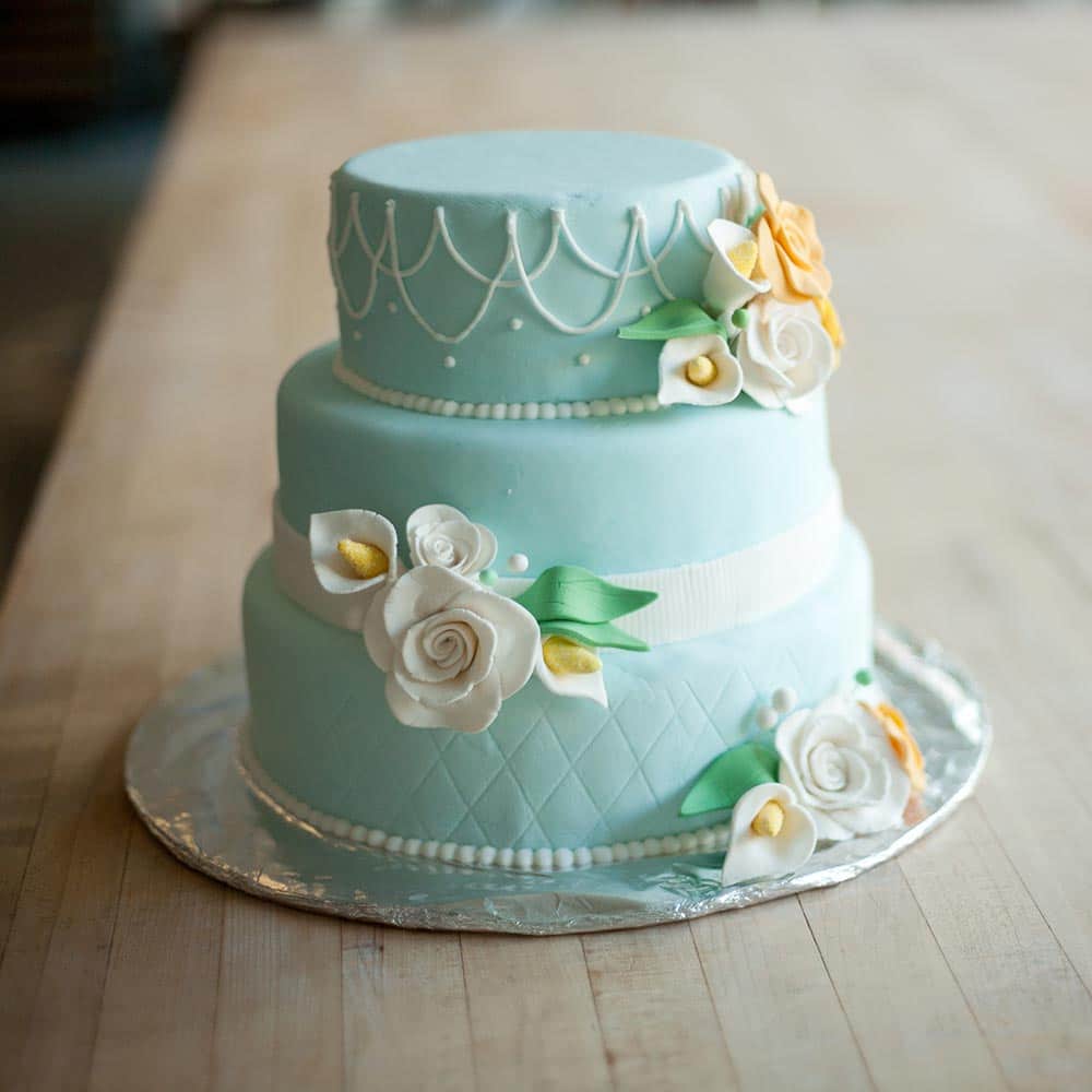 A three-tiered light blue fondant wedding cake decorated with white and yellow sugar flowers and delicate piping.