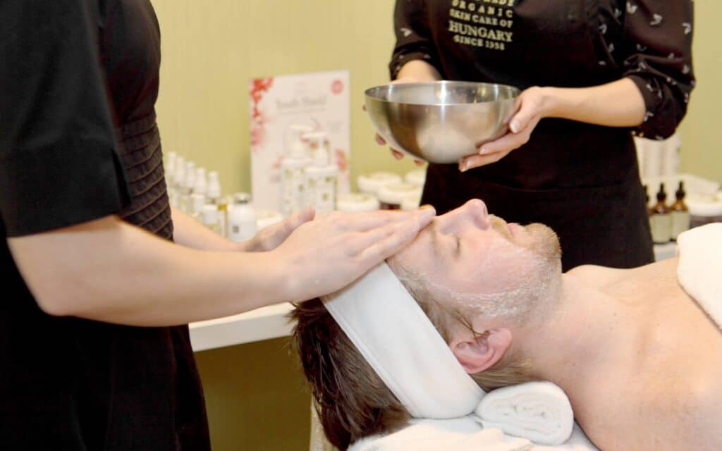 An aesthetician applies a facial treatment to a client wearing a white headband.