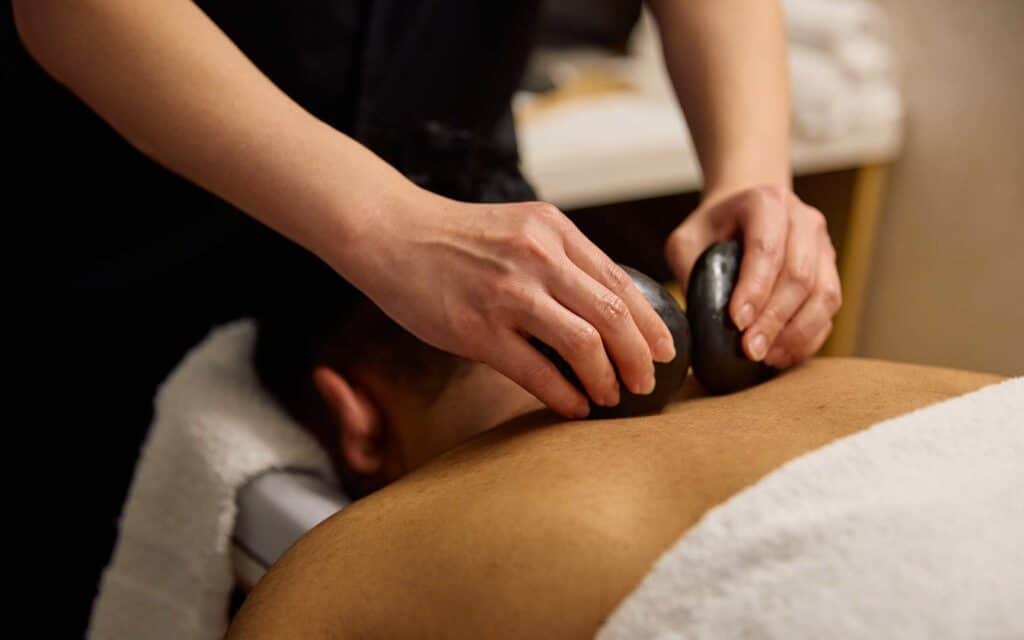 A massage therapist places smooth hot stones on a client's back for a spa treatment.