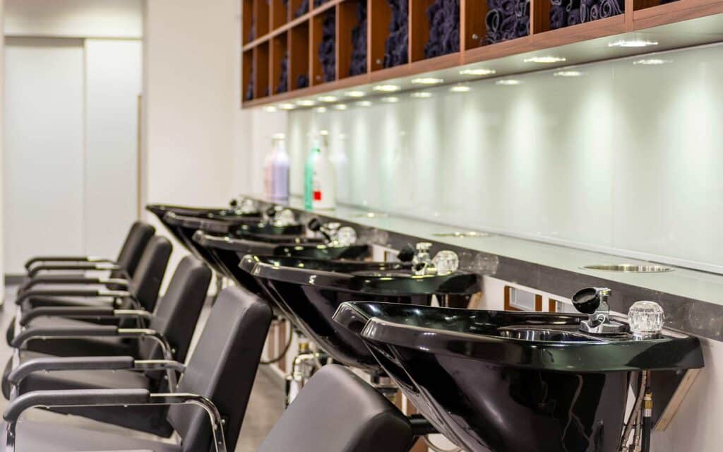 A row of black professional salon hair-washing sinks and chairs.