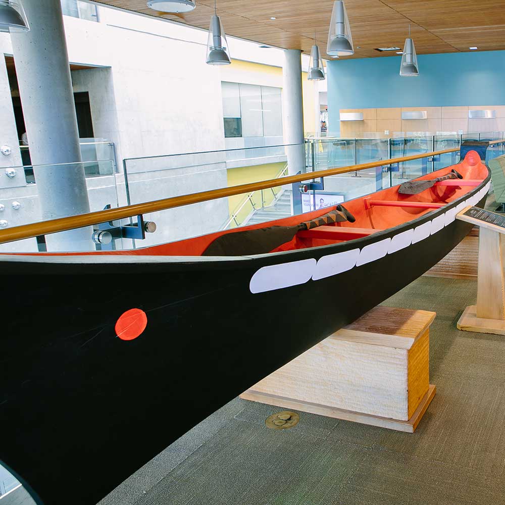 Indigenous art of a real size carved canoe in black and red and white with 2 wooden paddles