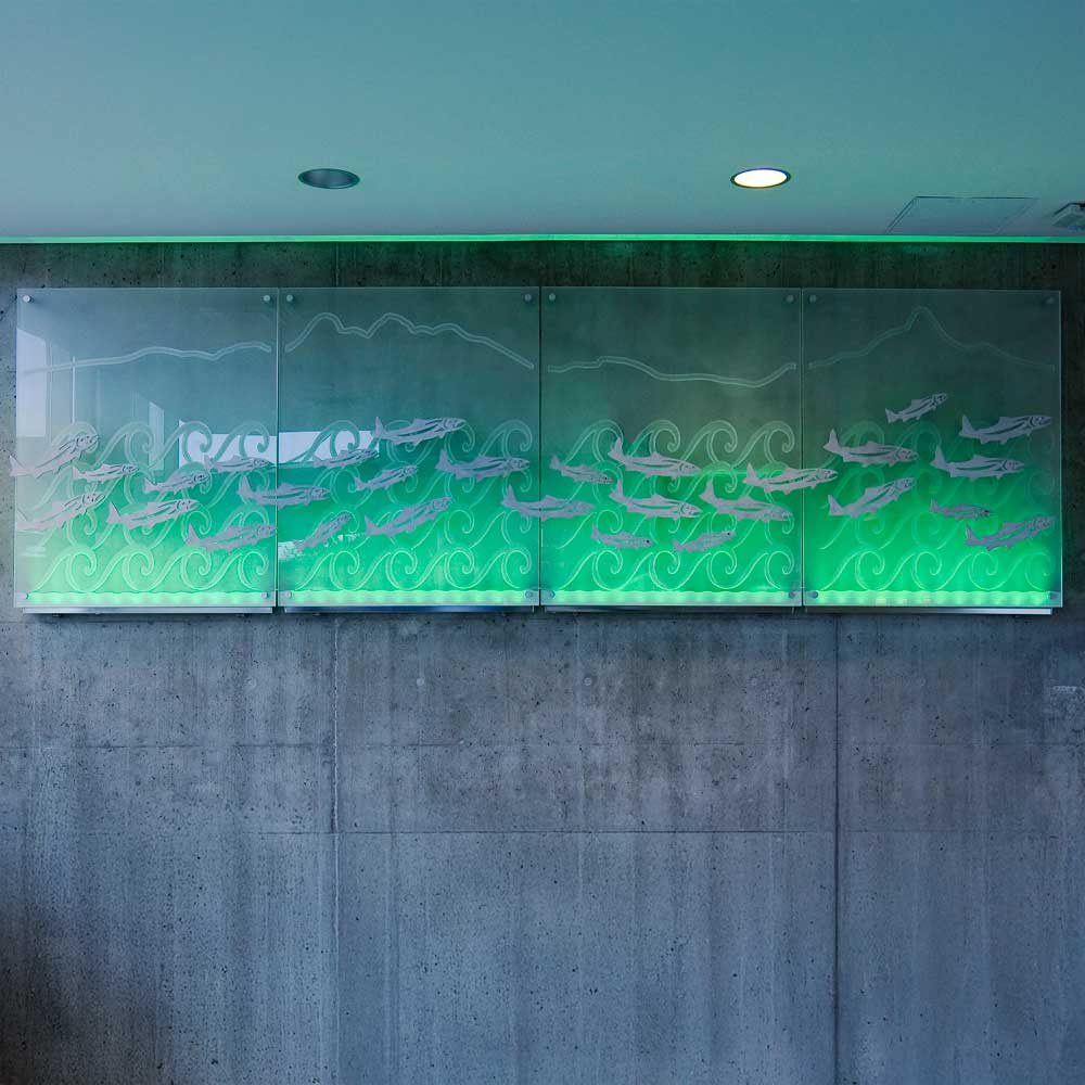 An indigenous art illuminated four glass panels with etched designs of fish and waves, backlit with green light.