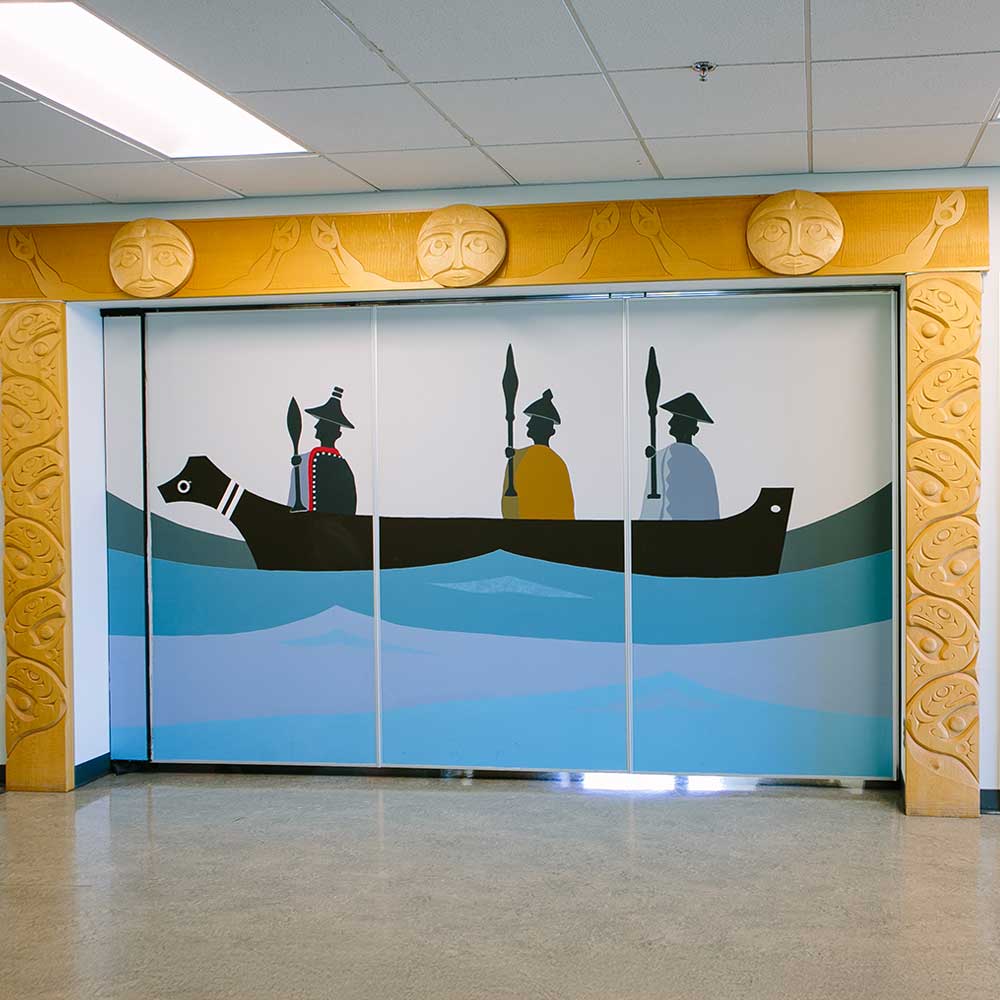 An indigenous art mural of a canoe in water with three people framed in a wooden carved fish and sun