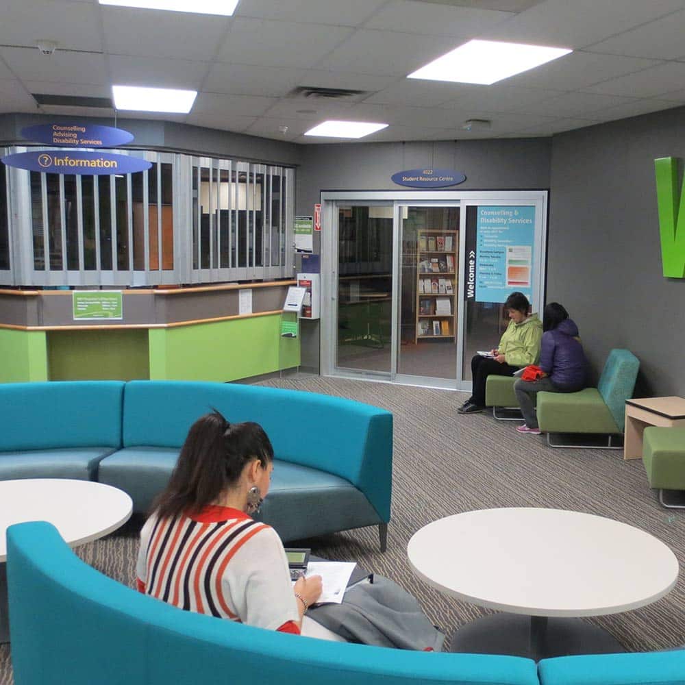 A modern student service center featuring curved blue seating and a dedicated information desk for counselling, advising, and disability services.
