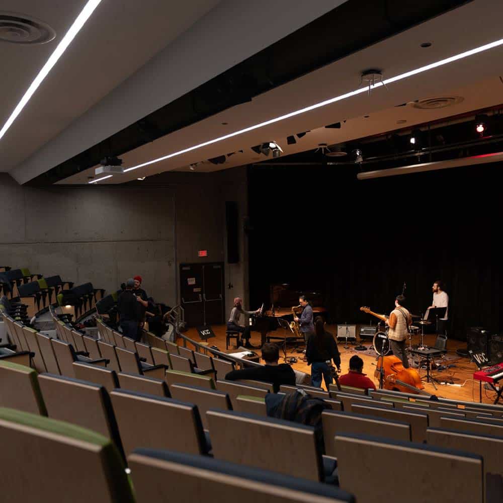 A tiered campus auditorium where a live student jazz ensemble performs on stage under professional lighting.