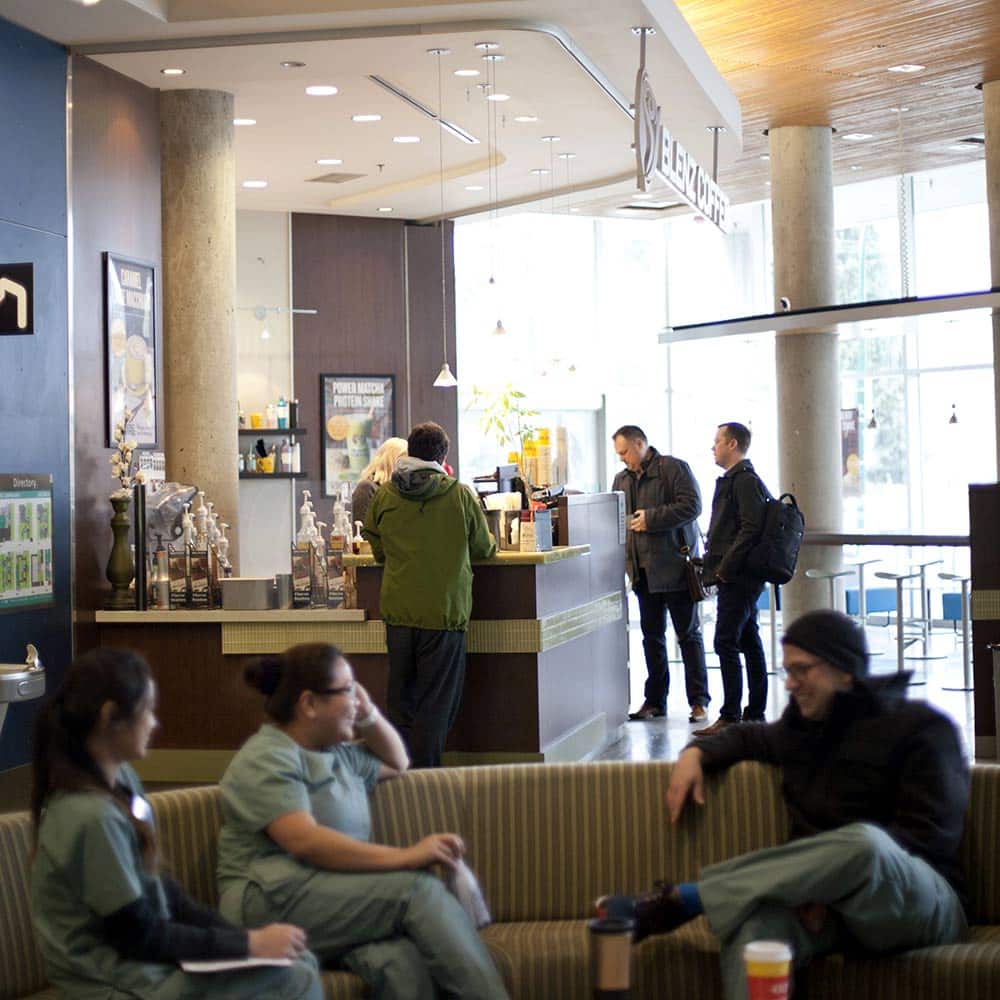 Students in nursing scrubs relax and socialize in a comfortable lounge area adjacent to the campus Blenz coffee shop.