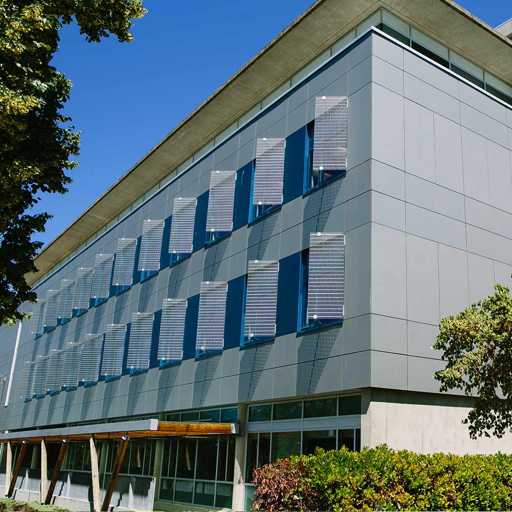 Modern facade of Building B features a series of geometric sunshades over rows of windows under a clear blue sky.
