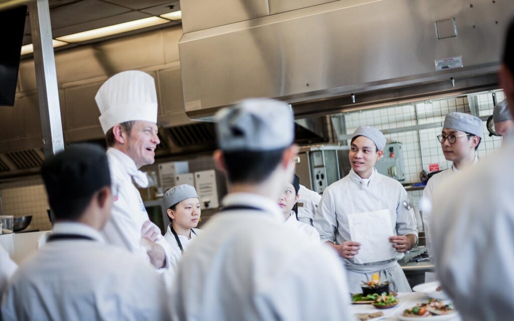 A chef instructor teaches students in a kitchen setting