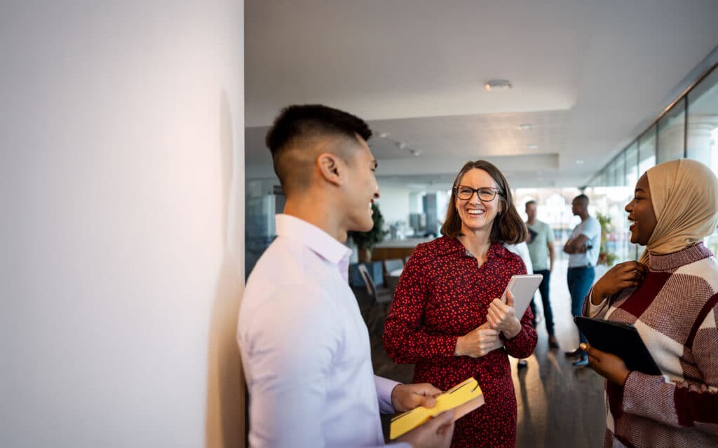 A diverse group of smiling professionals engages in a friendly conversation in a bright, open workspace.