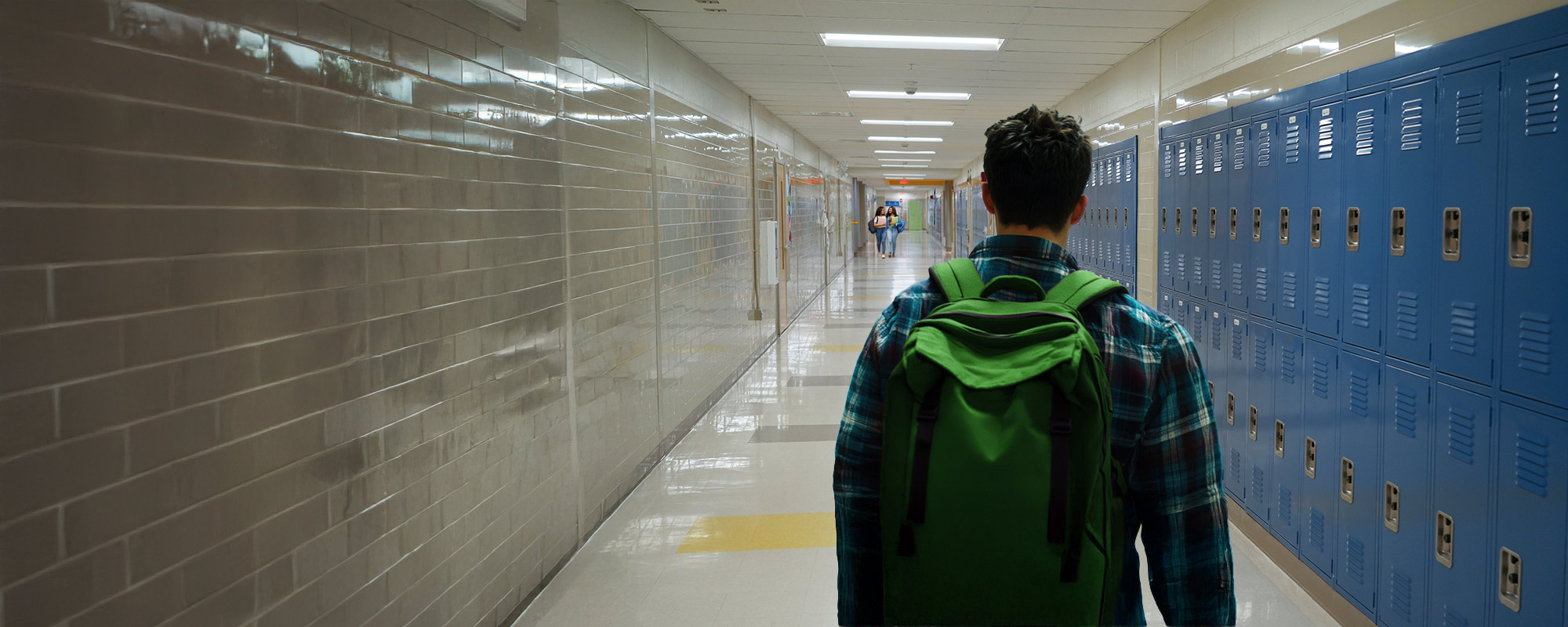 Student wearing a green backpack walking down a hallway