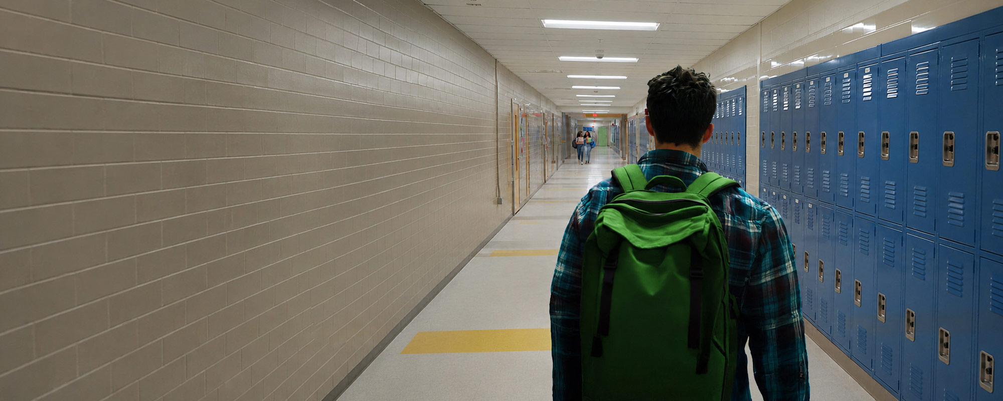 Student wearing a green backpack walking down a hallway