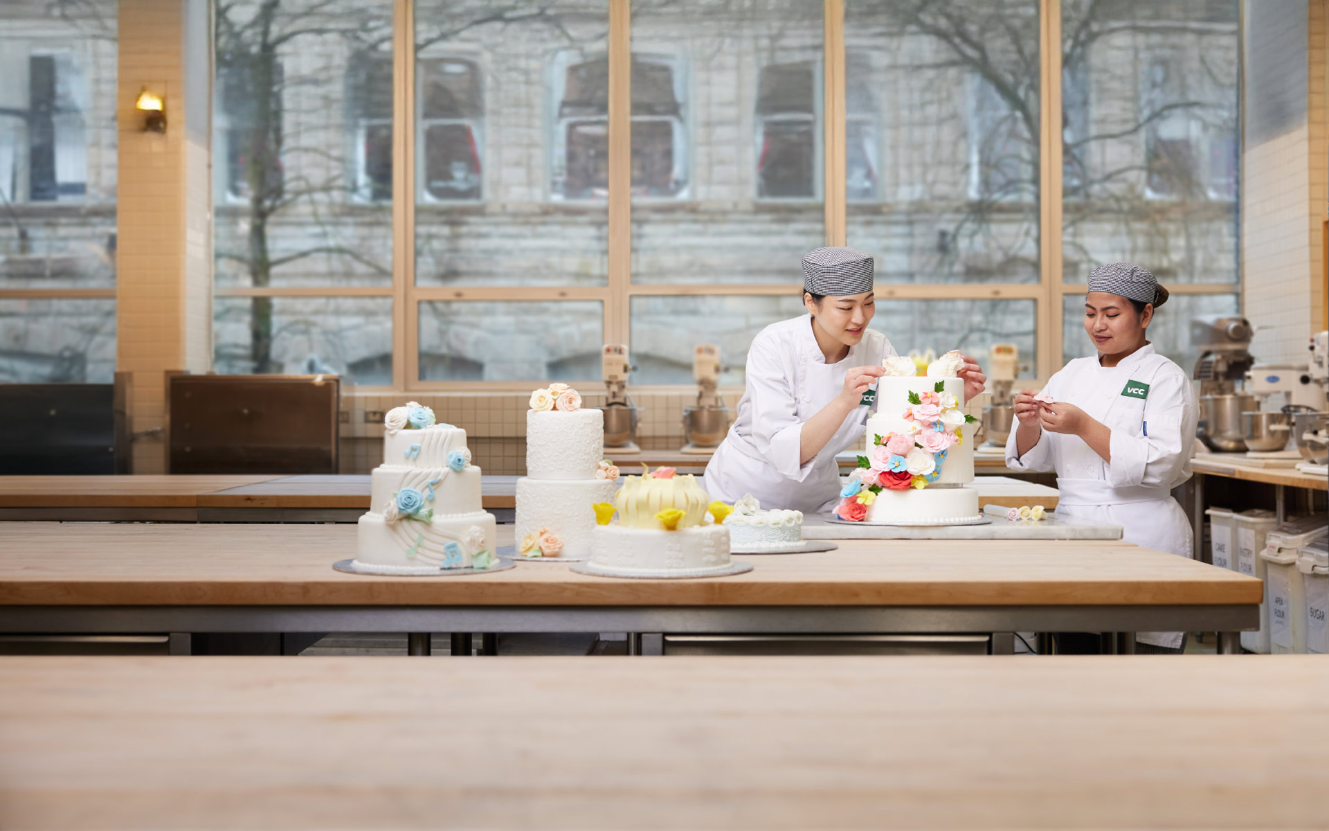 Two baking students decorating tiered wedding cakes