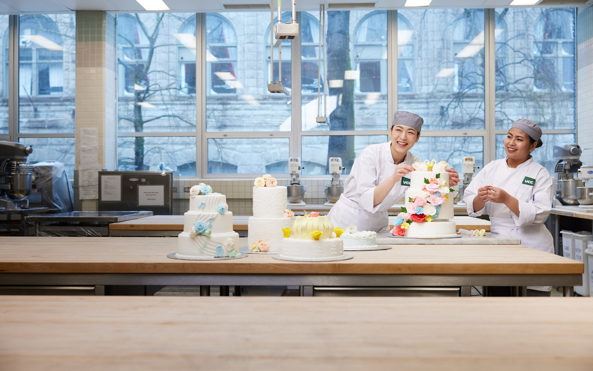 Two baking students decorating tiered wedding cakes