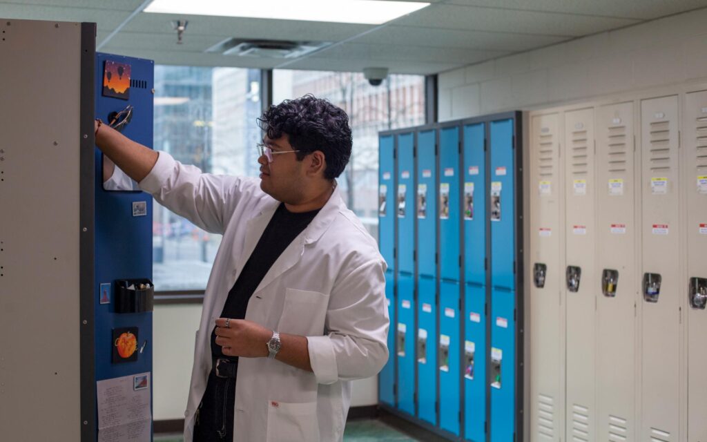 Student in a lab coat accessing a locker in a campus hallway