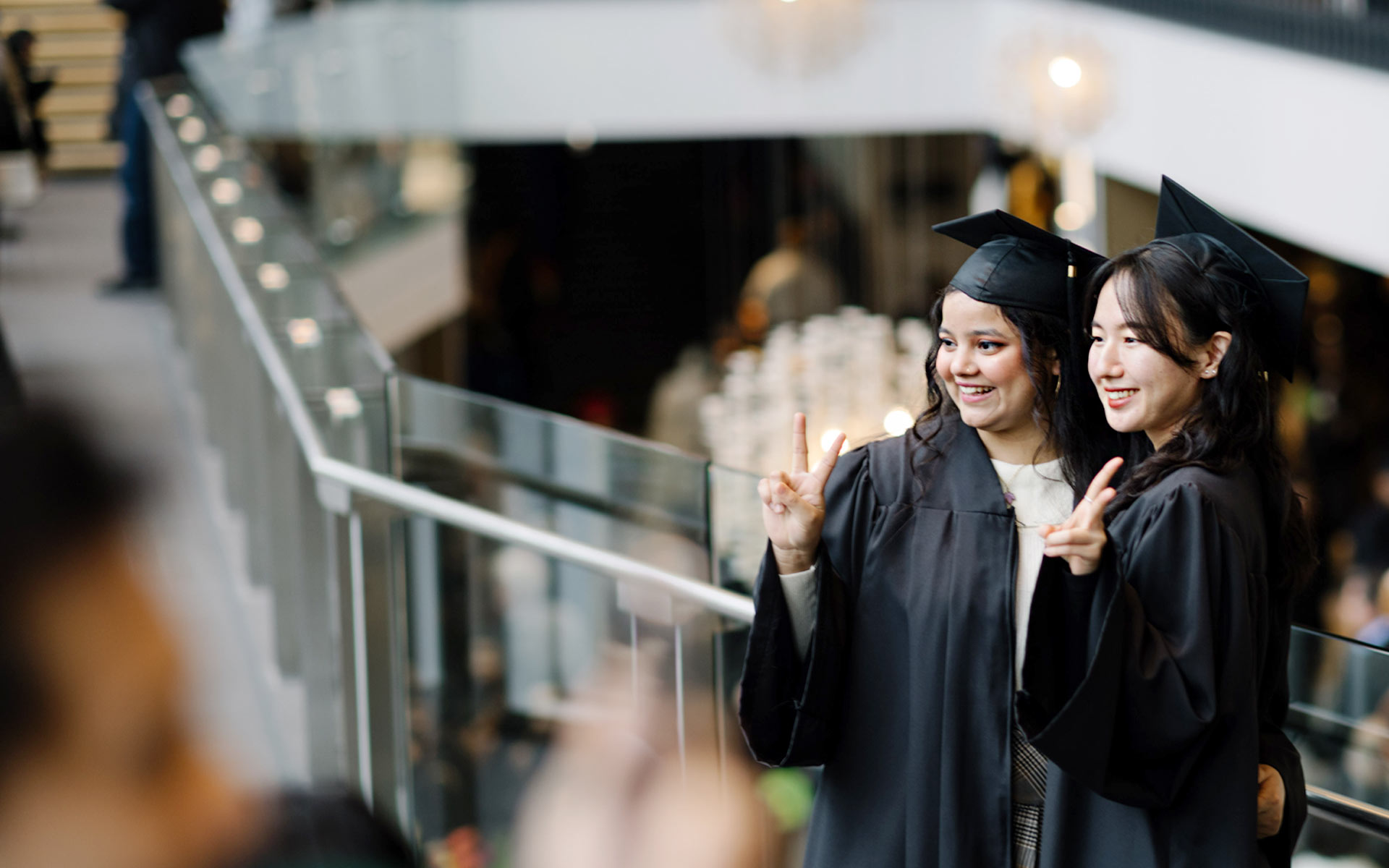 Two female graduates in full regalia posing at a camera.