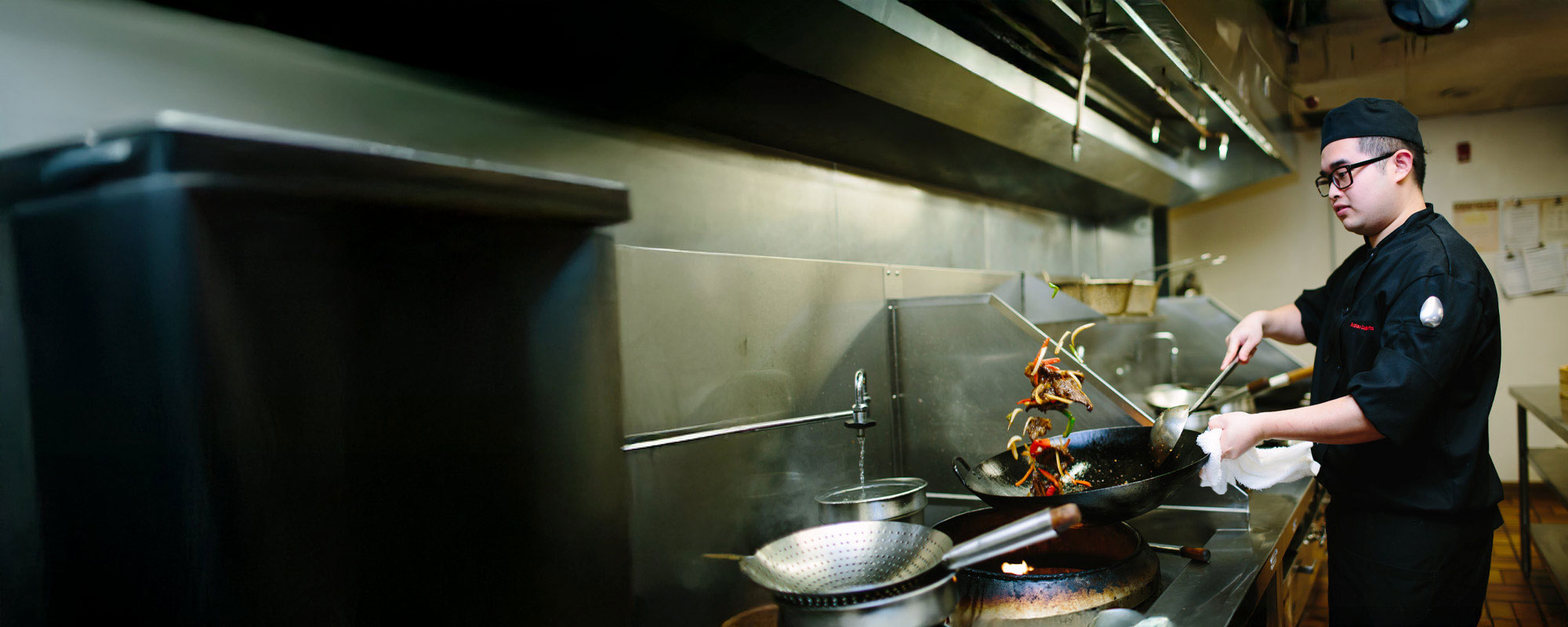chef skillfully tosses a stir-fry in a large wok, showcasing the dynamic energy of Asian culinary techniques in a commercial kitchen.