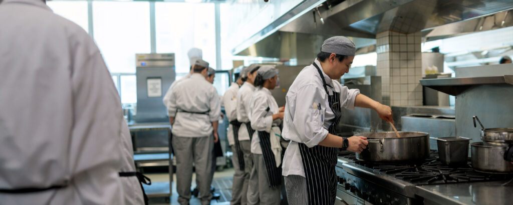 A team of culinary students in matching uniforms and striped aprons works together in a kitchen