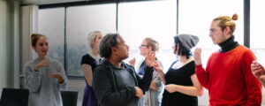 A small group of individuals stand together and communicate using sign language in a bright classroom setting.