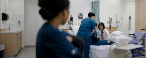 Health care assistant students practice patient transfer and care techniques under the guidance of an instructor in a clinical lab setting.