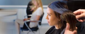 A hairstyling student gently brushes dark wet hair during a professional salon training session.